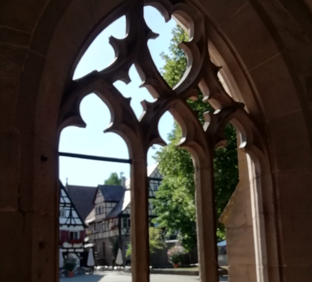 Blick durch gotisches Spitzbogen-Fenster auf einen historischen Marktplatz.